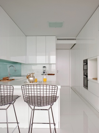 The kitchen receives ample sunlight, which reflects off the glossy white surfaces and Harry Bertoia barstools.