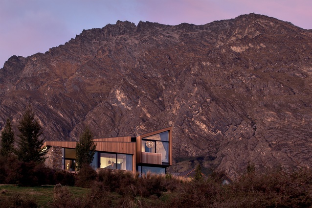 The cedar-clad house is dwarfed by the dramatic mountainous backdrop.
