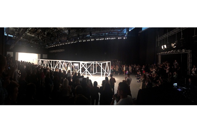 A sea of standing observers closely watch the first model engage with the defined catwalk space.
