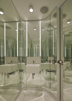 The powder room has green-hued glass curved around each wall, creating a jewel-like mirrored cocoon. 
