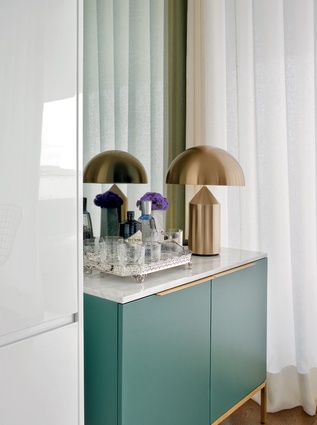 The small bar area in the kitchen, adorned with a Vico Magistretti lamp, features brass detailing and a mint-coloured finish to contrast with the room’s white, glossy surfaces. 