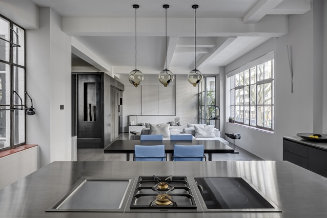 Beneath a triptych of bulbous pendant lights, a sleek monochrome kitchen flows into the open-plan living and dining zone.