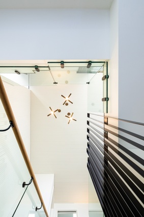 Three Petrine brass pendants from Nightworks Studio hang above the internal stair. Below them, the sculptural steel and glass balustrade.