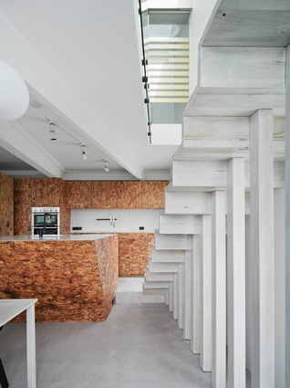 Within the open-plan space, the kitchen is differentiated with a elevated timber floor, while  a white skeleton stair creates a sculptural backdrop.