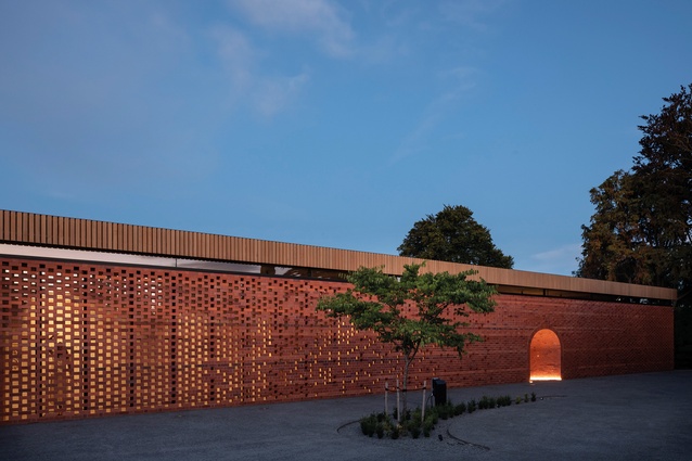 A long, perforated screen of carefully placed bricks creates a crafted façade through which entry is invited via a low arched opening.