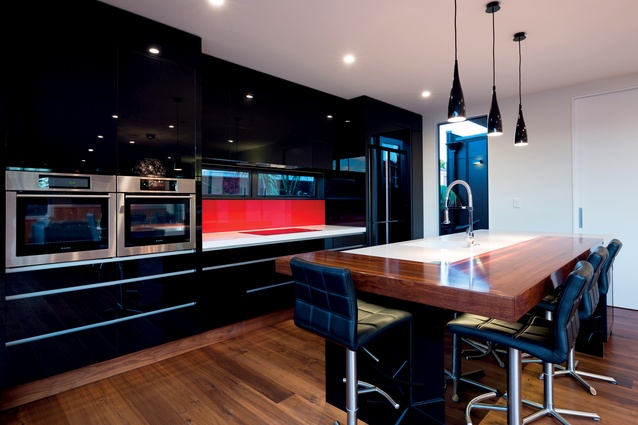Neutral walls provide a calming backdrop to the dramatic timber and black kitchen with its pop of red. 