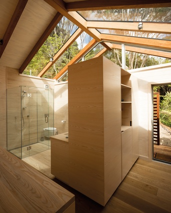 Glazing over the bathroom creates a light-filled space with a view of the sky and the treetops. Through the doorway is an external shower.
