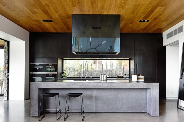 The sleek black kitchen has a lower ceiling than the living space; almost every transition from one space to another is marked by a change in ceiling height.

