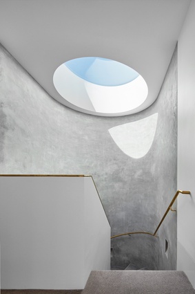 A dramatic circular skylight throws light onto the concrete wall of the spiral staircase.