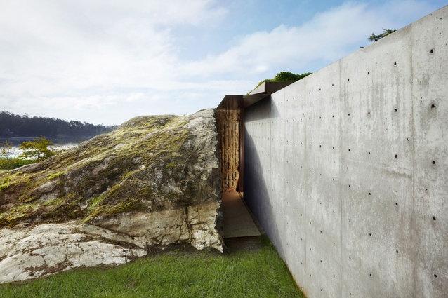 The entrance is a narrow and tall hallway sandwiched between the sliced-up boulder and a concrete wall. 