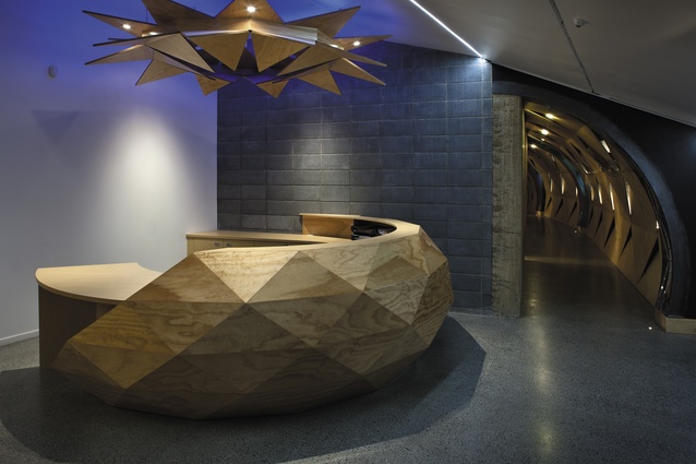 The multifaceted, bowl-shaped reception desk composed of plywood segments.