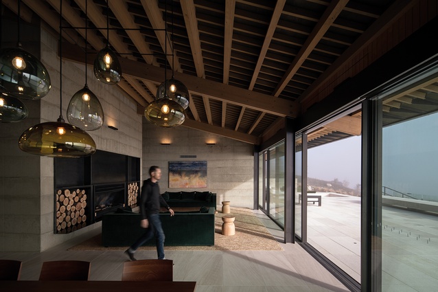 The building has exposed timber roof framing, in-situ poured concrete walls and a limestone-tiled terrace.