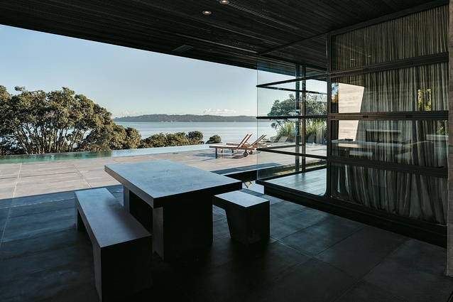 The outdoor living area with dining table, fireplace, waterfall pool and glass cabana.