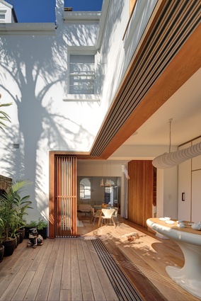 The timber screens and battens cast playful shadows across the kitchen, blurring the boundaries between inside and out.