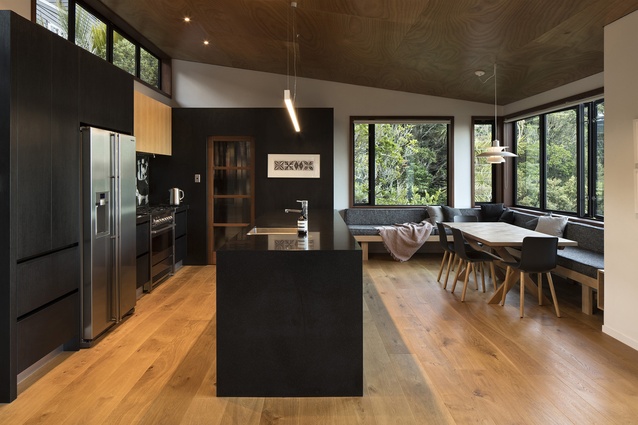 Whare Koa House, Mahurangi West, by SGA Architects. 2017. The kitchen of the home looks out onto the surrounding bush and features black cabinetry.