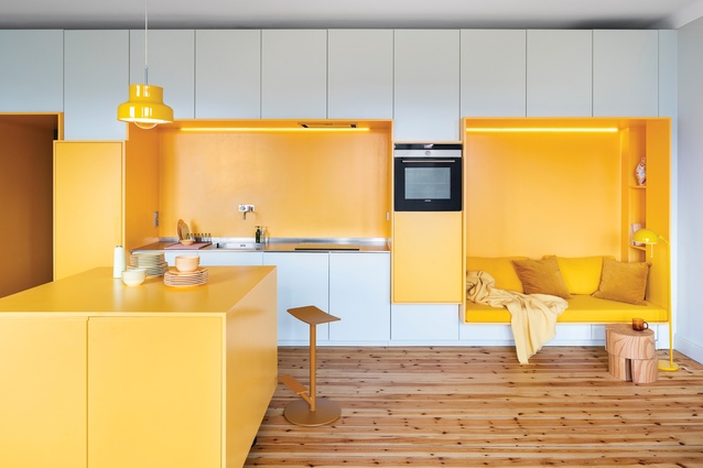 Egg-yolk-yellow finishes on the recessed seating alcove, bench and island unify the kitchen and dining space in a home by Lookofsky Architecture in Stockholm. 