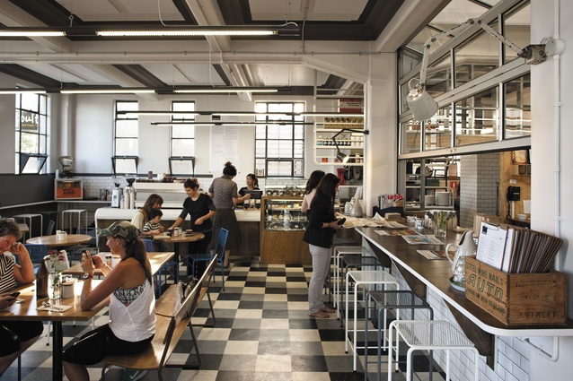 Interior view of Kokako café and coffee roastery. Floor-tile colouring is repeated in the graduated colours of the ceiling. Almost-invisible acoustic panels on the ceiling help suppress noise inside the ‘concrete bunker’.