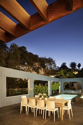 The pool area unfolds beneath an eye-catching blue wall with hexagonal patterning, with further concealment offered by the broad leaves of various palm trees dotted around the exterior.