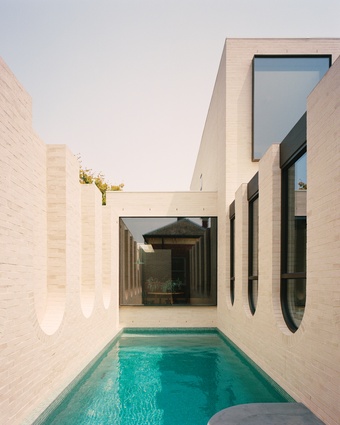 Distinctive inverted brick arches frame the edge of a swimming pool that is reminiscent of a Roman bathhouse.