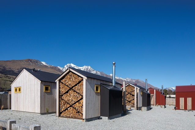 On the exterior of each hut, the wood-burner alcove reads as a lean-to. Some huts are timber clad, others steel clad; walls of stacked firewood give the simple buildings some textural heft.