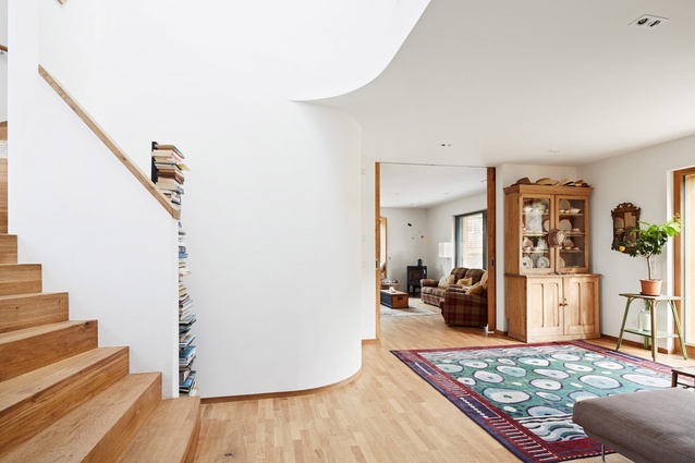House R, Cambridge. A staircase ascends through a double-height void, and the skylight above the curving inner wall ensures plenty of natural light enters the dining and lounge area.