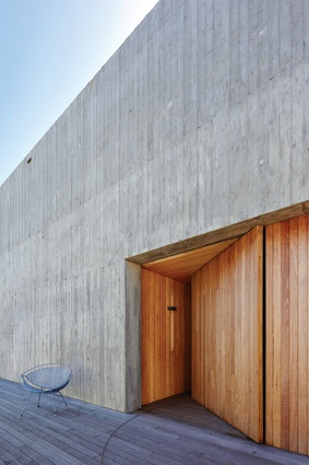 A pivot timber door marks the south-facing entry within the textured in situ concrete wall.