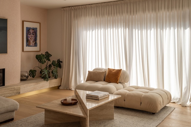 A curved stucco wall surrounds the fireplace, with a travertine ledge on either side. Long curtains cover the eight metres of window joinery and soften the space.