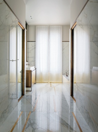 The bathroom appears luxurious with the floor-to-ceiling marble and brass veins and bespoke cabinetry. 