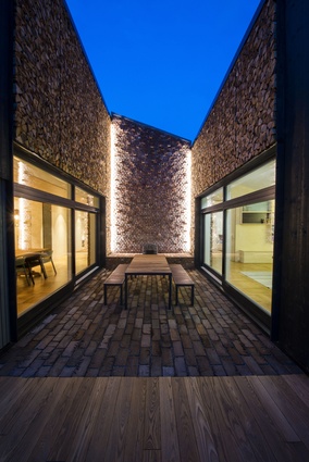 A small, sheltered courtyard that can be used for outside dining in moderate weather is  surrounded by walls made of stacked firewood and brick.