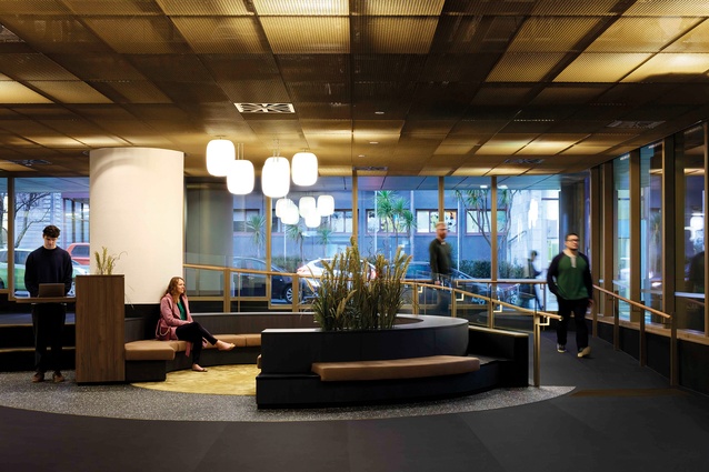 Dark floors and gold mesh ceiling above frame the ground-floor lobby as a special public ātea.
