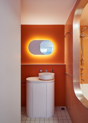 Orange accents, seen boldly in the bathroom and more subtly elsewhere, form a counterpoint to the otherwise monochromatic palette.