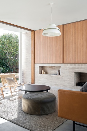 Rowlock brick steps rise to the second pavilion where large sliding glass doors and a skeletal white frame diminish the barriers between the living room and landscape.