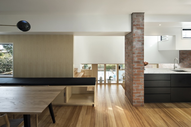 A bench seat runs beyond the dining room towards a brick wall and creates a portal to the stairway. Floors in this new part of the home are recycled kauri.
