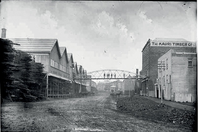Auckland Timber Company Building (right), after its takeover by the Kauri Timber Company in 1888, looking east. A wire suspension bridge hosted rails to allow the transfer of goods from the factory to the mill on trollies. 