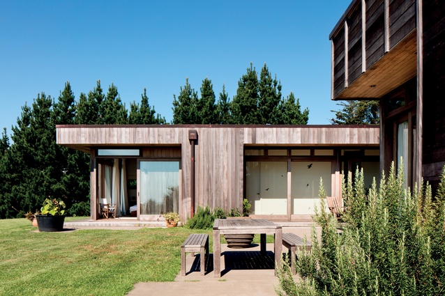 The pavilion-like form is clad in weathered cedar and totara wood with copper detailing.
