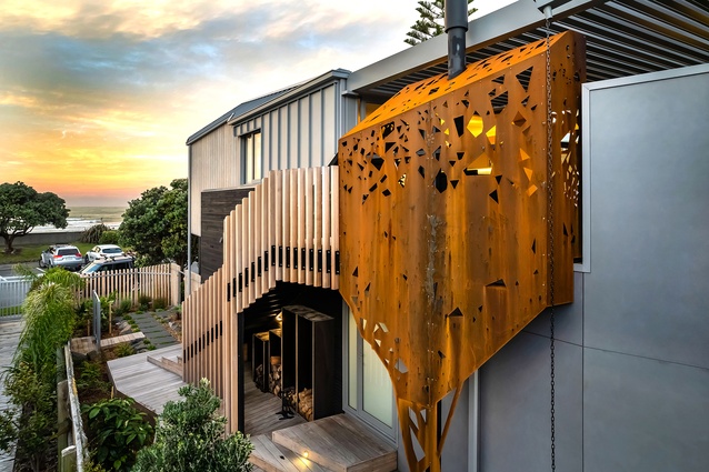 A splash of corten steel breaks up the cedar and metal cladding, enveloping an outdoor fireplace setting off the kitchen.