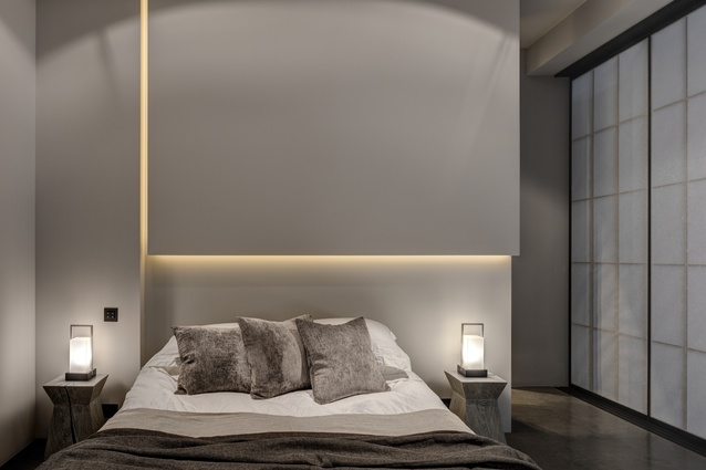 In the bedroom, a sculptural vertical bulkhead above the bed conceals subtle illumination in narrow slots.