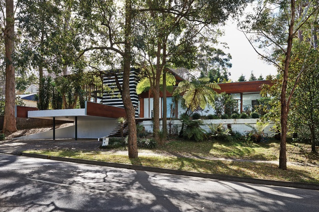 The house has become a Sydney landmark for its two dramatic gestures to the street – the cantilevered deck over the carport and the two-storey volume of stairs enclosed by a screen in forest-green and white stripes.