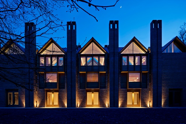 The New Library, Magdalene College in Cambridge by Níall McLaughlin Architects. The gabled roofs and chimneys of the exterior are lit up at dusk.