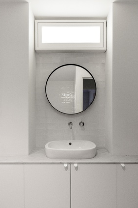 The lack of windows in the bathroom is countered with glossy tiles and mirrors that bounce light and an opaque light box.

