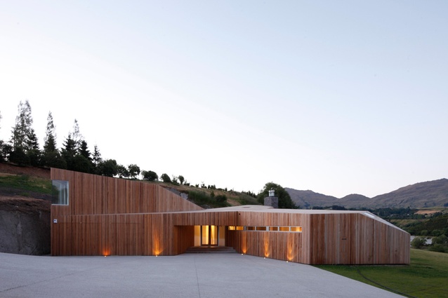The cedar skin seamlessly envelops the entire form, making walls and roof read as a single, unified object.