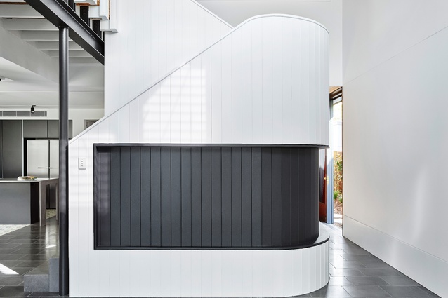 Wrapped in white vertical joint boards, the stair is a solid, sculptural object that divides living from dining spaces.