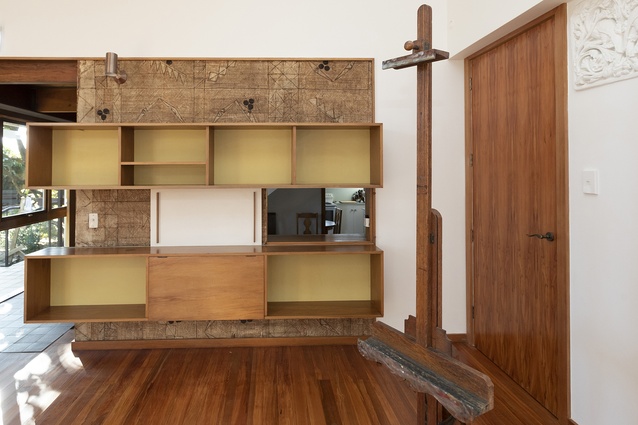 East wall of studio, showing tapa cloth backing, shelves and hatch to kitchen. 