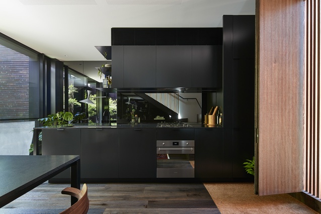 Mirror-lined, black-tinted walls and kitchen splashback extend the visual depth of the tight space.