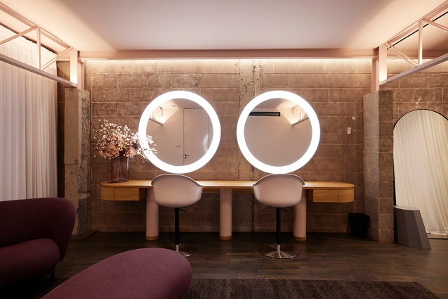 Upstairs, the hair and makeup area and talent lounge feature utilitarian concrete walls juxtaposed with rounded timber joinery and light-edged round mirrors. To contrast the industrial elements, soft curtains provide privacy and distinct colours to define zones.