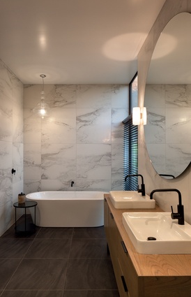 The bathroom features marble, wood and black tapware. A giant circular mirror makes the space appear larger.
