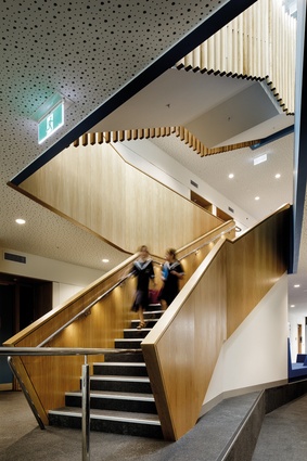 The robust timber staircase connects levels around a glazed atrium within the performing arts school.