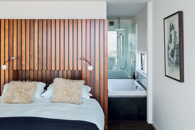 The master bedroom has an en suite and a headboard that copies the wood of the central stairway.