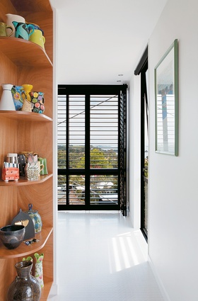 In the open passageway that leads to the master bedroom, ceramics are displayed on built-in ply shelving.
