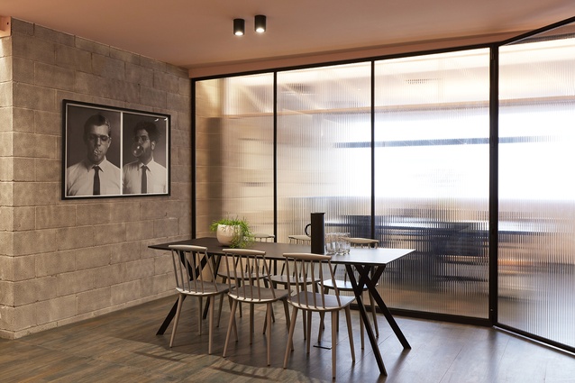 The upstairs meeting room is framed by fluted glass. A blush-pink ceiling highlight or conceals the building's existing features selectively and a sandblasted finish has been applied to the existing concrete block walls.